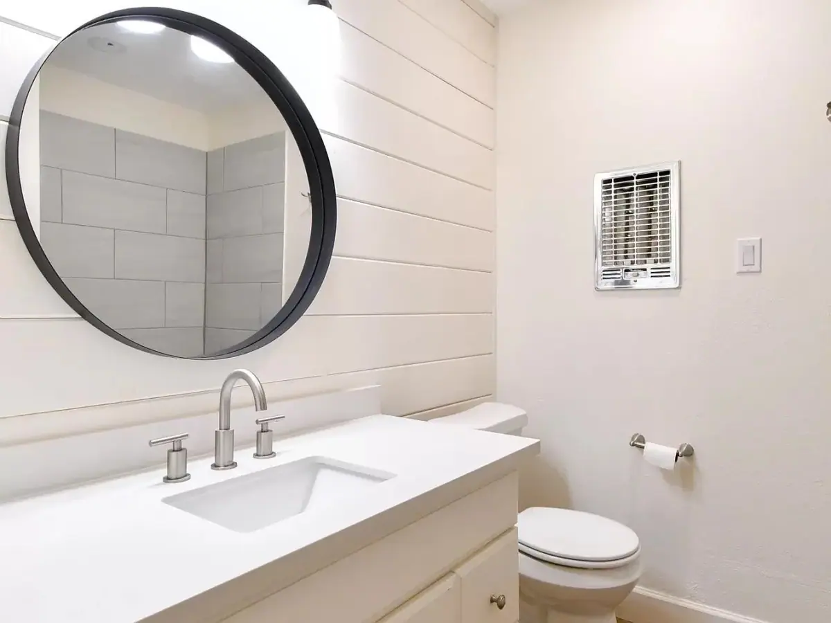 Bathroom with a round mirror, shiplap wall and white vanity