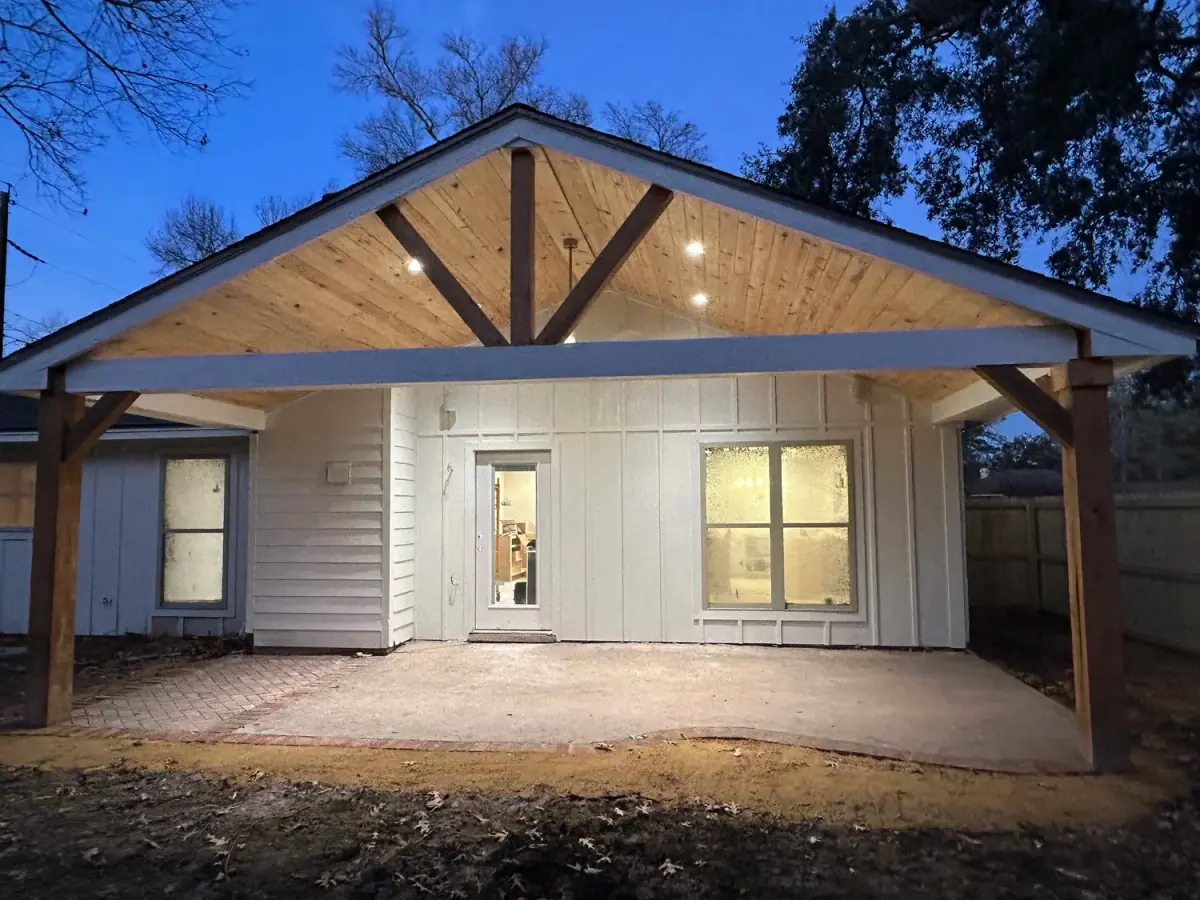 Gable patio cover tied into a board-and-batten house, lit at night
