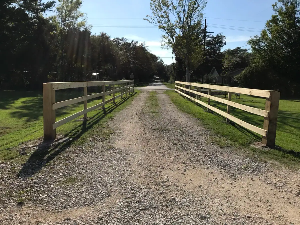 Three-rail ranch fence along a gravel drive