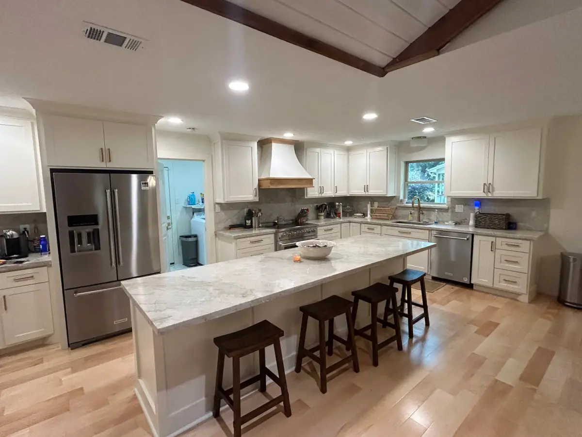 Remodeled kitchen with white shaker cabinets, a long quartz island with stools and a wood floor