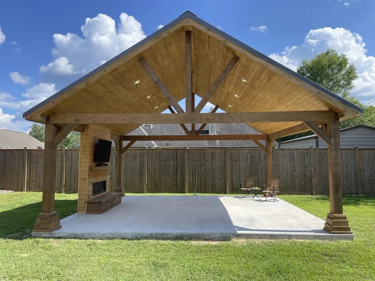 Gable pavilion with a stone outdoor fireplace and concrete slab in a fenced yard
