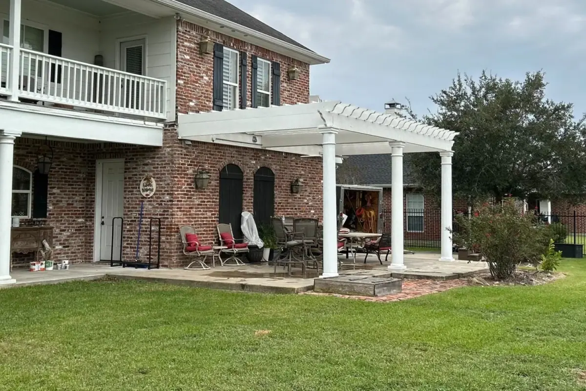 White painted pergola on round columns against a brick two-story house